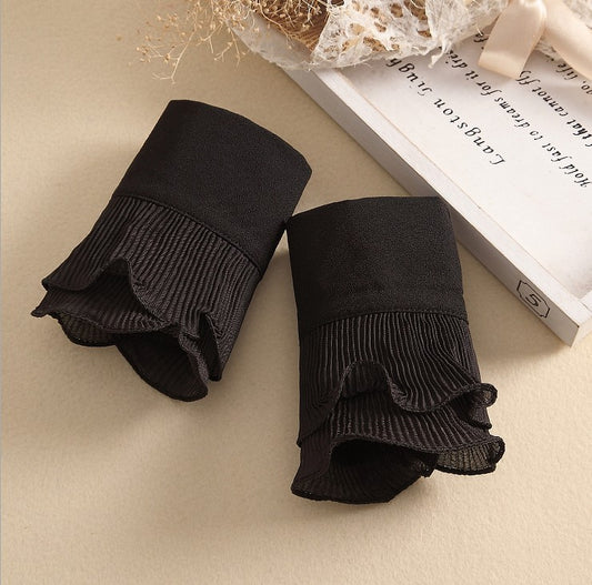 Pair of black ruffled socks on a beige surface with a book in the background.