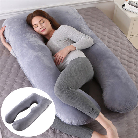 Woman lying on a large U-shaped gray pillow on a bed.