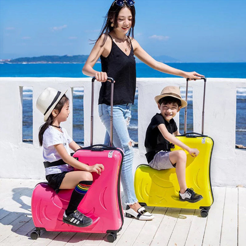 Woman with two children sitting on pink and yellow suitcases by a waterfront.