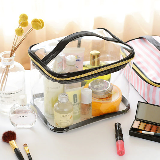 Clear makeup bag with black zipper containing various skincare and cosmetic products on a white surface.