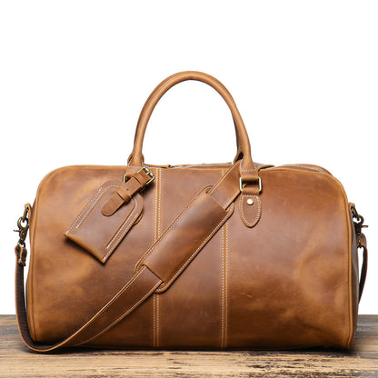 Brown leather duffel bag on a wooden surface with a white background